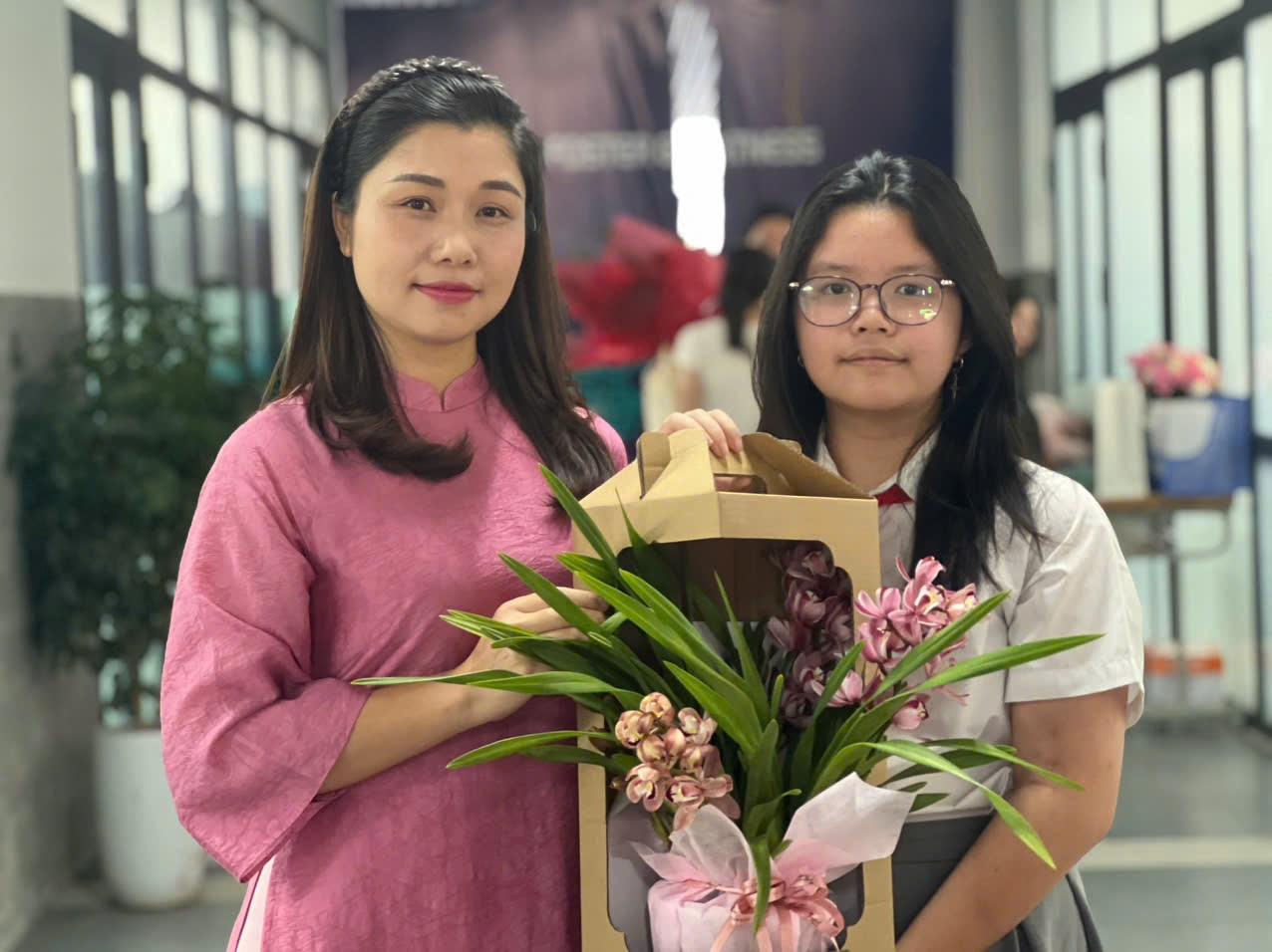 Two women holding flowers and a box of flowersAI-generated content may be incorrect.