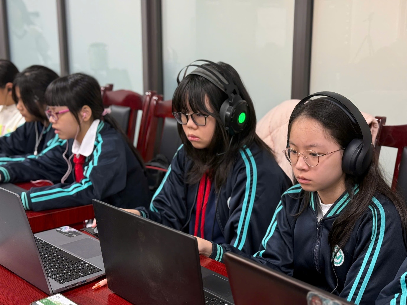 A group of girls sitting at a desk with laptopsAI-generated content may be incorrect.