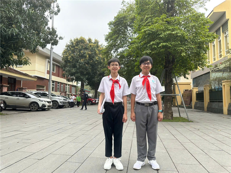 Two boys wearing school uniforms and standing on a sidewalkAI-generated content may be incorrect.