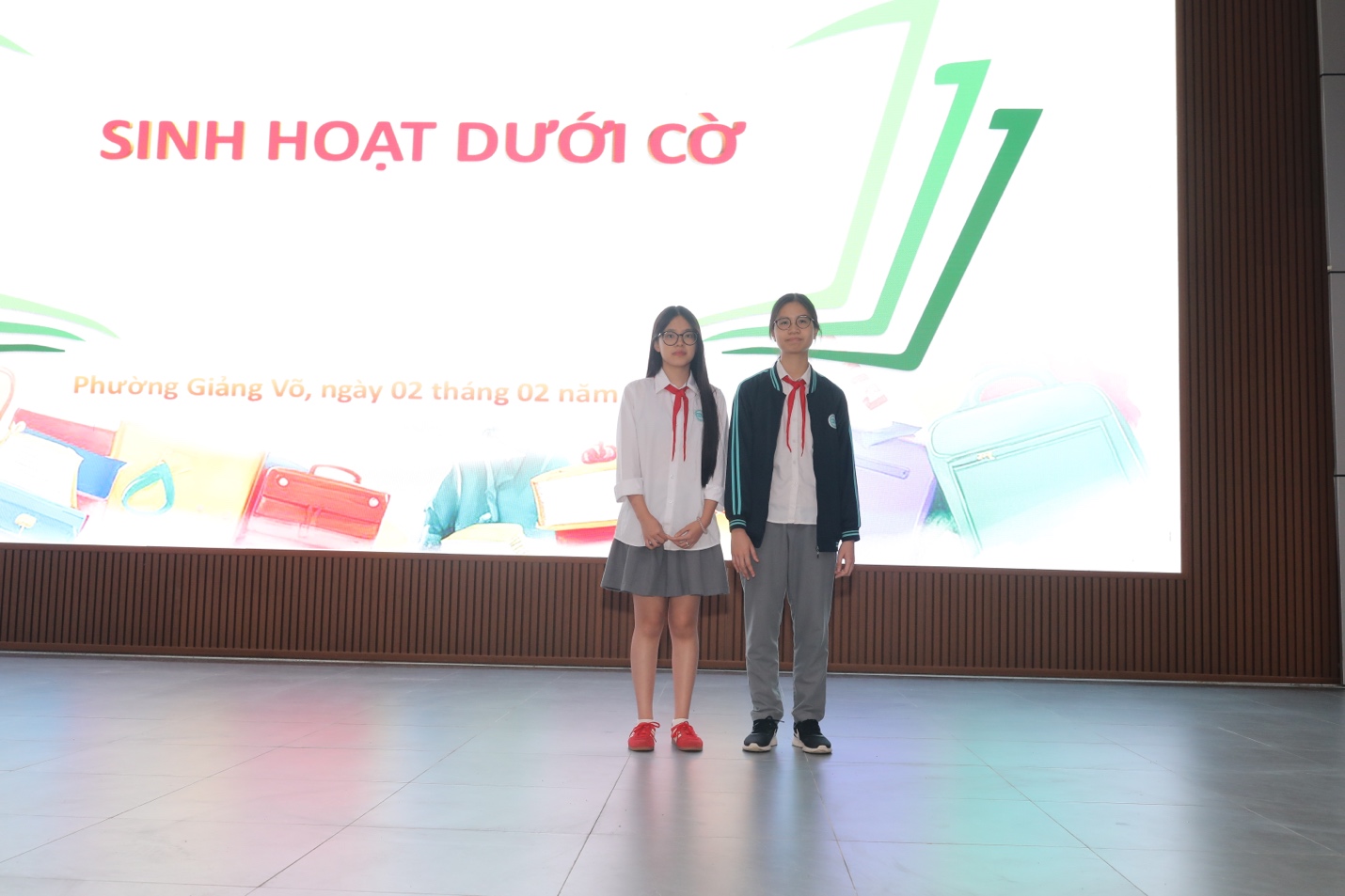 A couple of young people standing in front of a large screenDescription automatically generated